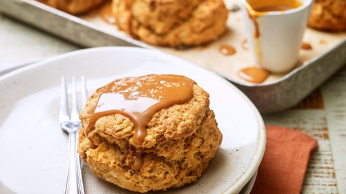 A salted caramel and butternut squash scone on white plate with more scones in the background on a baking tray